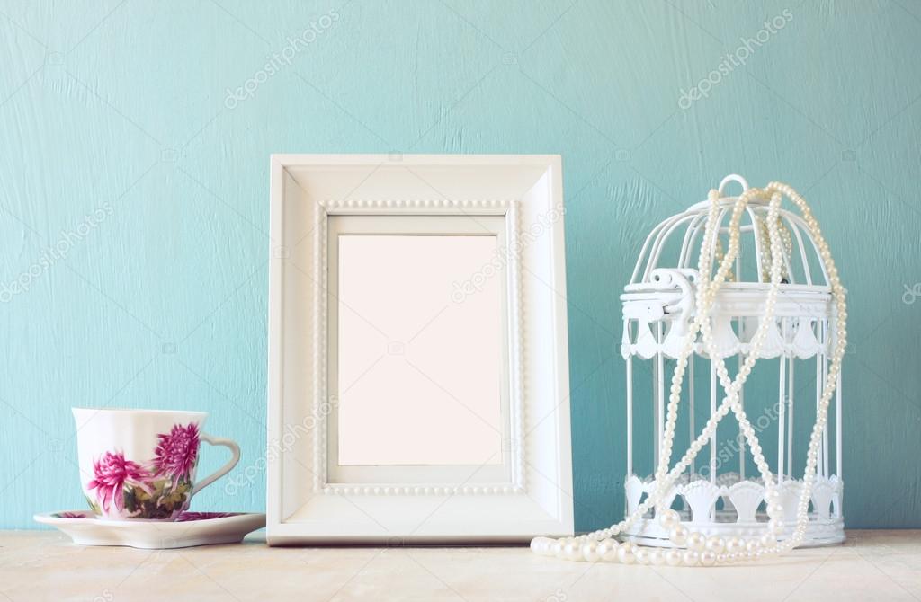 Vintage classical white frame on wooden table with porcelain cup and lantern