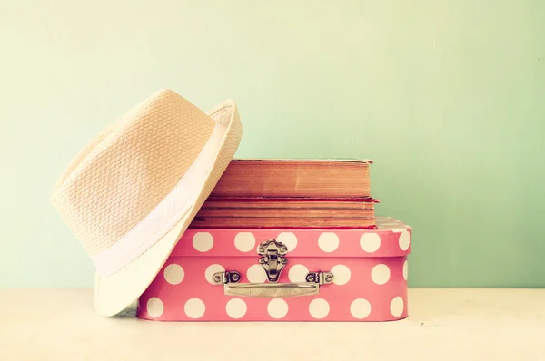 Foto de mala rosa com bolinhas, chapéu fedora e pilha de livros sobre mesa de madeira, imagem estilo retro — Fotografia de Stock