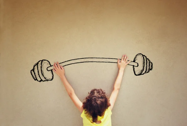 Photo of kid's back view lifting up barbell weights against textured background — Stock Photo, Image