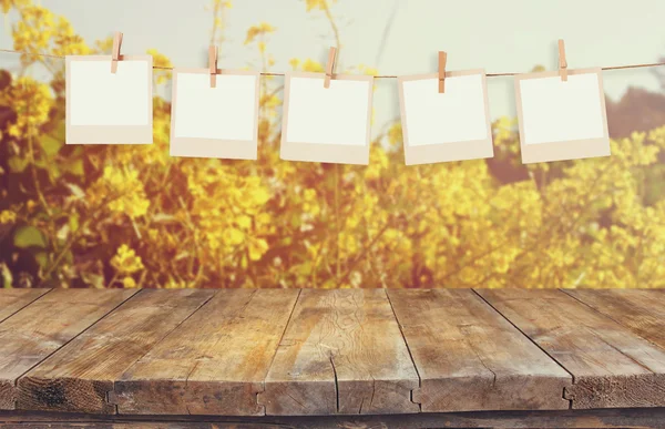 Gamla polaroid foto ramar hnaging på ett rep med vintage träskiva bord framför sommar blommor fält bloom landskap med bländning — Stockfoto