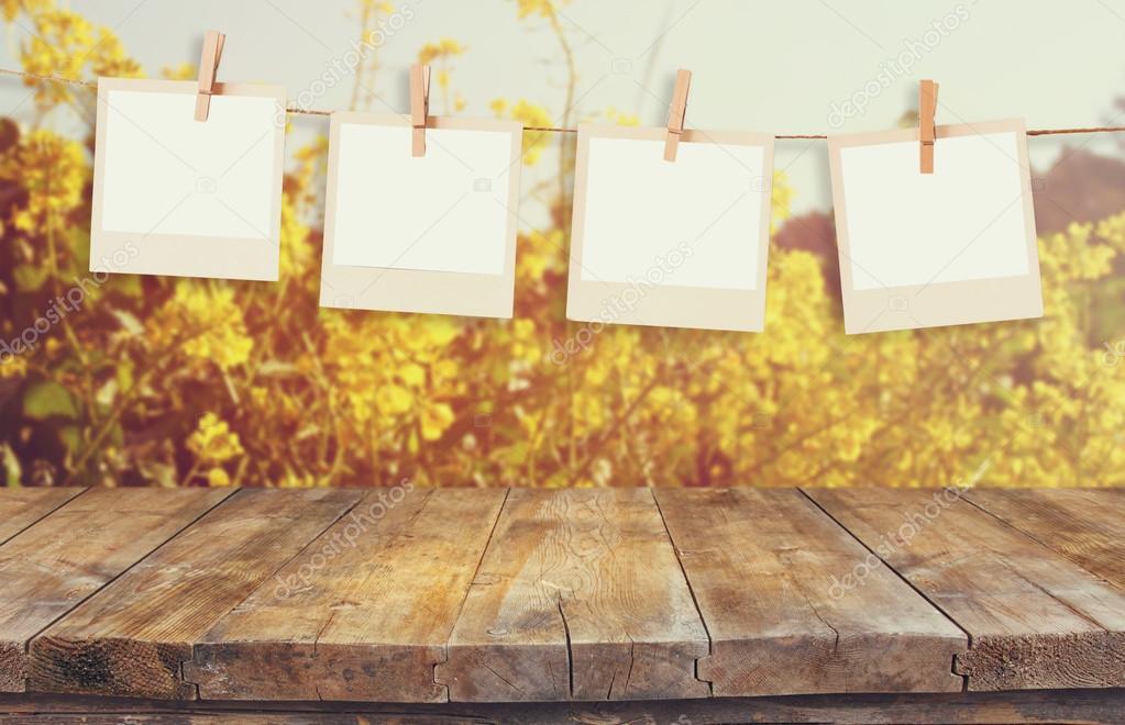 old polaroid photo frames hnaging on a rope with vintage wooden board table in front of summer flowers field bloom landscape with lens flare