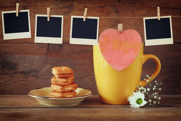Κορνίζες φωτογραφιών που κρέμεται από ένα σκοινί με φλιτζάνι καφέ και μπισκότα, πέρα από το ξύλινο υπόβαθρο — Φωτογραφία Αρχείου