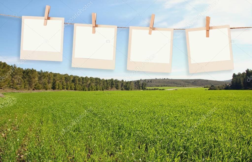 Old polaroid photo frames hanging on a rope in front of open field landscape background