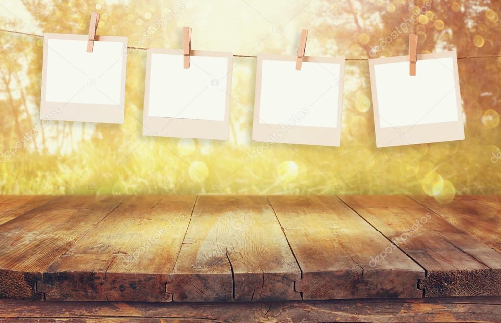 Old polaroid photo frames hanging on a rope with vintage wooden board table in front of abstract forest landscape