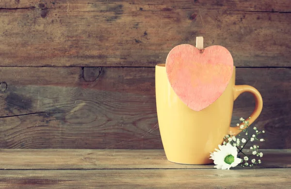 Mag amarillo con un corazón rosa vintage de madera en la mesa de madera — Foto de Stock
