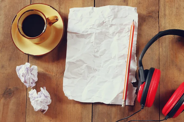 Bovenaanzicht beeld van verfrommeld papier naast hoofdtelefoons en kopje koffie over houten tafel — Stockfoto