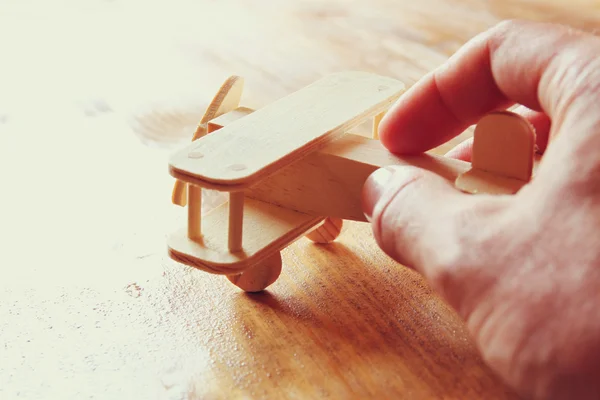 Close up foto da mão do homem segurando avião de brinquedo de madeira sobre fundo de madeira. imagem filtrada. conceito de aspiração e simplicidade — Fotografia de Stock