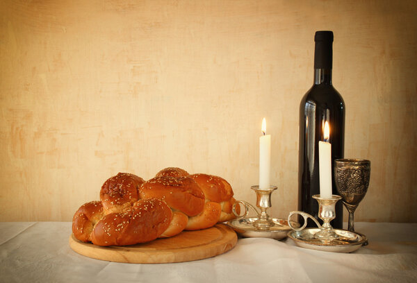 shabbat image. challah bread, shabbat wine and candelas on wooden table. vintage filtered image