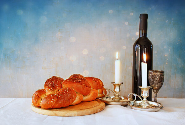 shabbat image. challah bread, shabbat wine and candelas on wooden table. glitter overlay