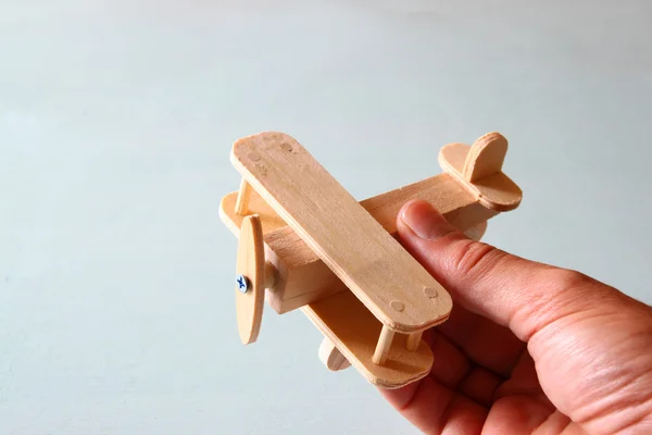 Foto ravvicinata della mano dell'uomo che tiene aeroplano giocattolo di legno su sfondo di legno. immagine filtrata. aspirazione e semplicità concetto — Foto Stock