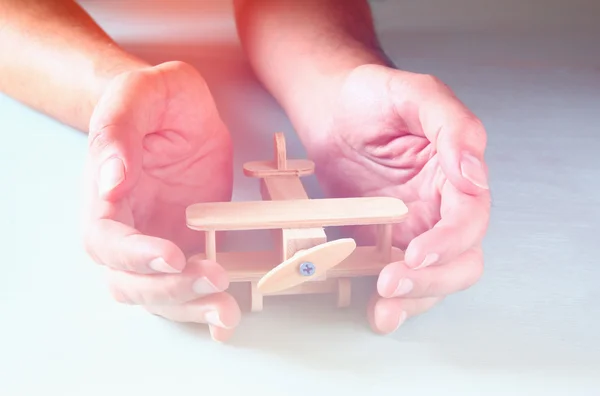 Close up photo of man's hand holding wooden toy airplane over wooden background. filtered image. aspiration and simplicity concept — Stock Photo, Image