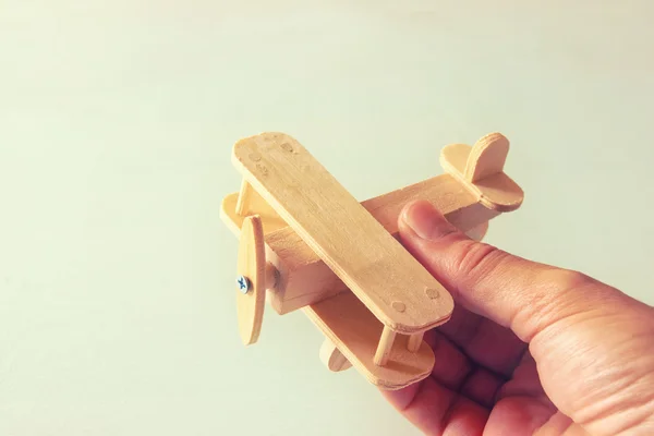 Foto ravvicinata della mano dell'uomo che tiene aeroplano giocattolo di legno su sfondo di legno. immagine filtrata. aspirazione e semplicità concetto — Foto Stock