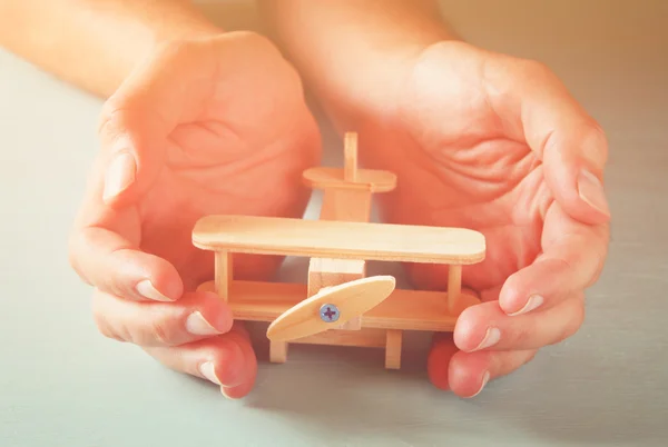 Close up photo of man's hand holding wooden toy airplane over wooden background. filtered image. aspiration and simplicity concept — Stock Photo, Image