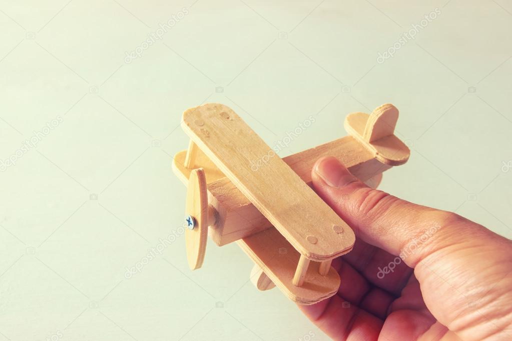 close up photo of man's hand holding wooden toy airplane over wooden background. filtered image. aspiration and simplicity concept