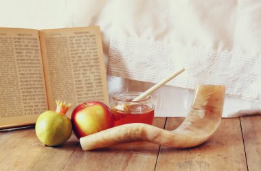 rosh hashanah (jewesh holiday) concept - shofar, torah book, honey, apple and pomegranate over wooden table. traditional holiday symbols.