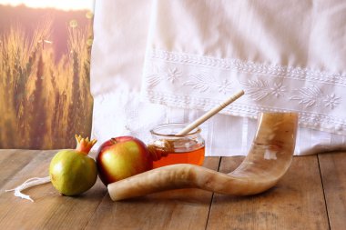rosh hashanah (jewesh holiday) concept - shofar, torah book, honey, apple and pomegranate over wooden table. traditional holiday symbols.