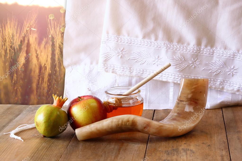 rosh hashanah (jewesh holiday) concept - shofar, torah book, honey, apple and pomegranate over wooden table. traditional holiday symbols.