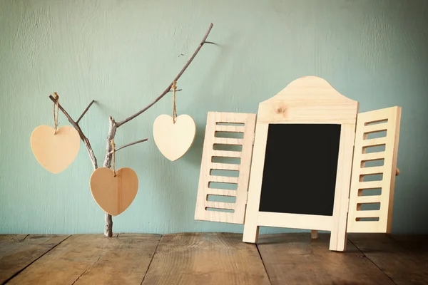 Quadro chalkboard decorativo e corações de madeira pendurados sobre mesa de madeira. pronto para texto ou mockup — Fotografia de Stock
