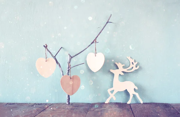 Hanging wooden hearts over and wooden rain deer decoration over wooden background. retro filtered image — Stock Photo, Image