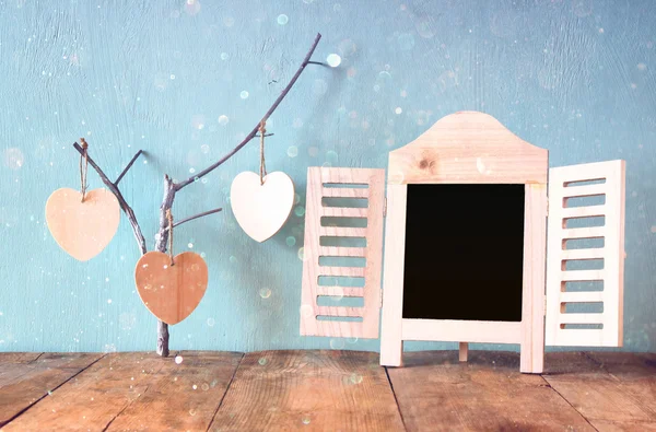 Decorative chalkboard frame and wooden hanging hearts over wooden table. ready for text or mockup. retro filtered image — Stock Photo, Image