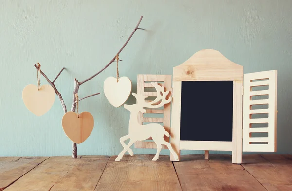 Marco de pizarra decorativa y corazones colgantes de madera sobre la mesa de madera. listo para texto o maqueta. imagen filtrada retro — Foto de Stock