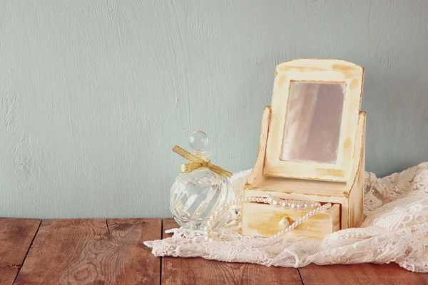 vintage pearls , antique wooden jewelry box with mirror and perfume bottle on wooden table. filtered image