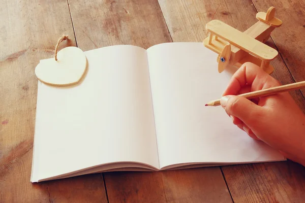 Caderno em branco aberto e mãos de mulher ao lado de avião de brinquedo na mesa de madeira. imagem filtrada estilo retro — Fotografia de Stock
