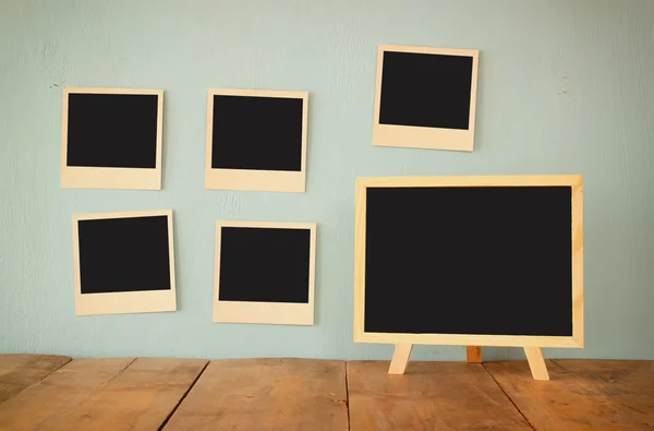 Blank instant photos hang over wooden textured background next to blank blackboard — Φωτογραφία Αρχείου