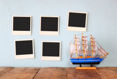 instant photos hang over wooden textured background next to decorative boat. retro filtered image