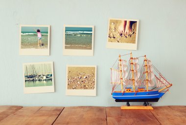 instant photos hang over wooden textured background next to decorative boat. retro filtered image
