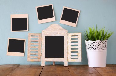blank instant photos hang over wooden textured background next to blank blackboard and flowerpot