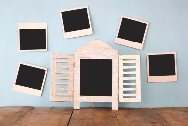 blank instant photos hang over wooden textured background next to blank blackboard