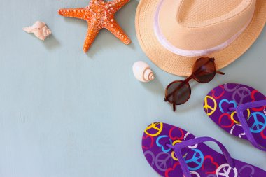 colorful flip flops, starfish, shells, fedora hat and sunglasses on wooden background