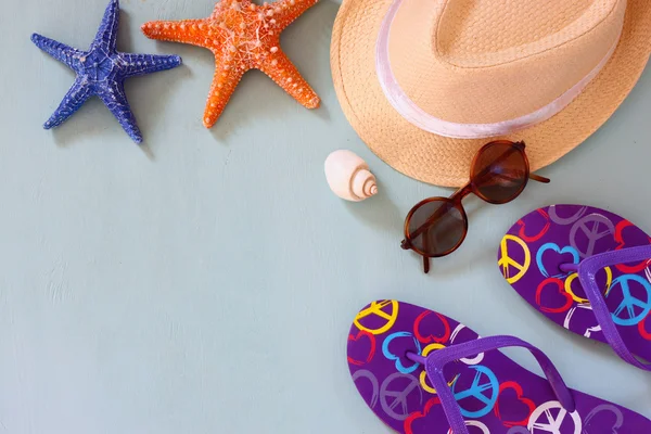 colorful flip flops, starfish, shells, fedora hat and sunglasses on wooden background