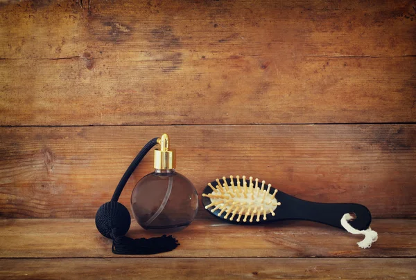 Photo of vintage perfume bottle next to old wooden hairbrush on wooden table. retro filtered image — Stock Photo, Image