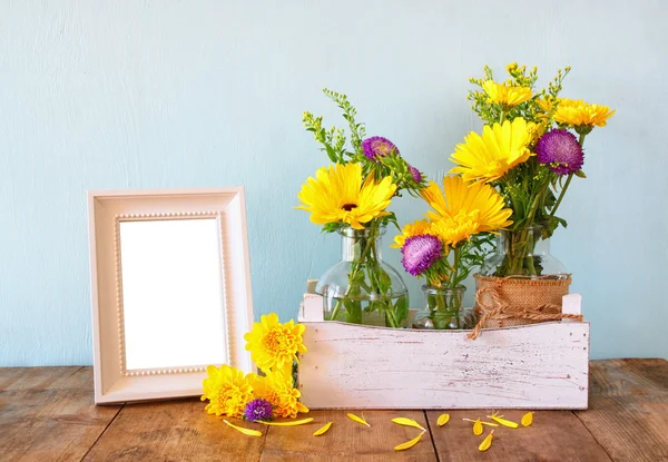 Sommerblumenstrauß neben leerem Vintage-Fotorahmen auf dem Holztisch mit Minzhintergrund. Vintage gefiltertes Bild — Stockfoto