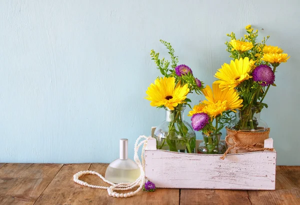Bouquet estivo di fiori accanto alla bottiglia di profumo e collana di perle sul tavolo di legno con sfondo menta. immagine filtrata vintage — Foto Stock