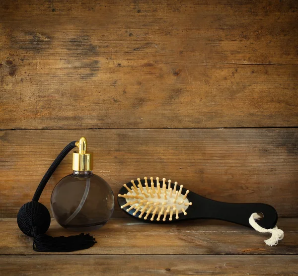 Photo of vintage perfume bottle next to old wooden hairbrush on wooden table. retro filtered image — Stock Photo, Image