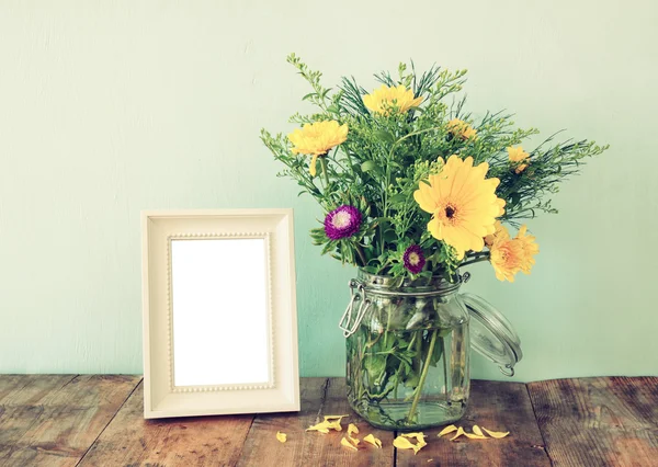 Ramo de flores de verano junto al marco de fotografía vintage en blanco en la mesa de madera con fondo de menta. vintage imagen filtrada — Foto de Stock