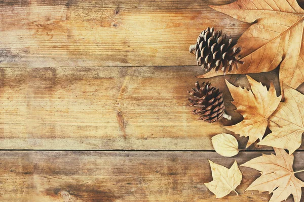 Imagen vista superior de hojas de otoño y conos de pino sobre fondo texturizado de madera . —  Fotos de Stock