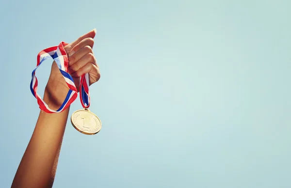 Mão mulher levantada, segurando medalha de ouro contra o céu. conceito de prêmio e vitória. — Fotografia de Stock