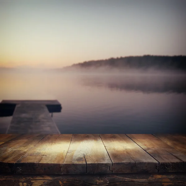 Vintage wooden board table in front of abstract photo of misty and foggy lake at morning sunrise — Stock Photo, Image