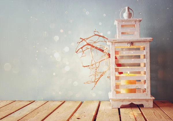 White wooden vintage lantern with burning candle and tree branches on wooden table. retro filtered image with glitter overlay. — Stock Photo, Image