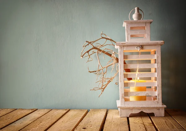 Low key image of white wooden vintage lantern with burning candle and tree branches on wooden table. retro filtered image. — Stock Photo, Image