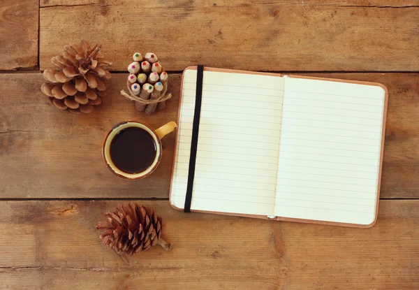 Imagem superior de notebook aberto com páginas em branco, ao lado de cones de pinho e xícara de café sobre mesa de madeira. imagem retro filtrada . — Fotografia de Stock