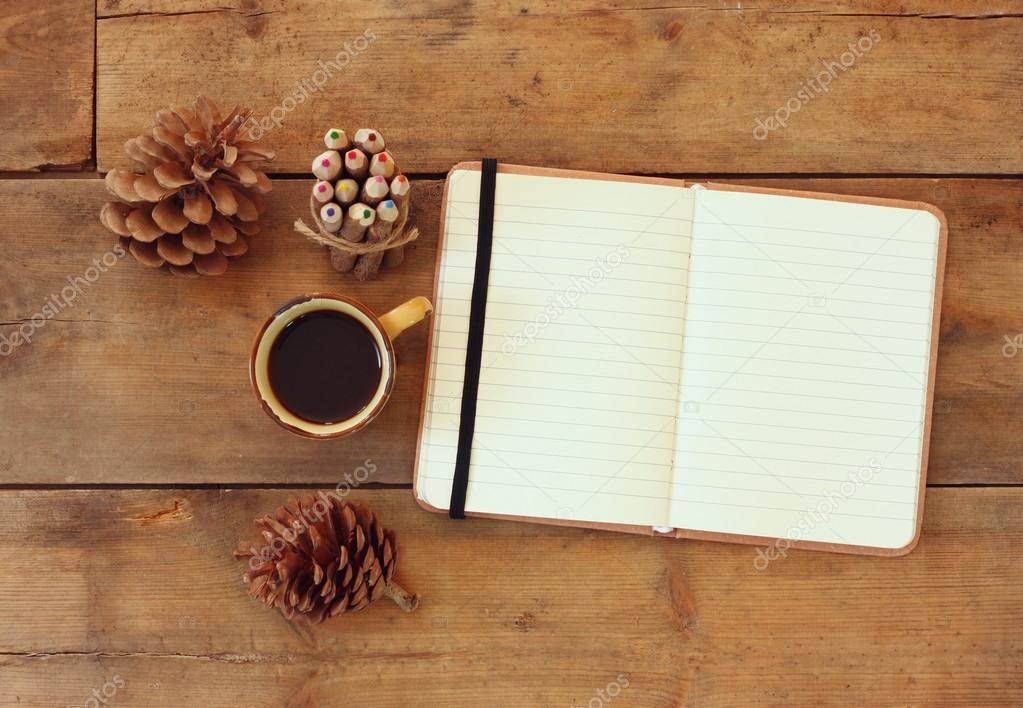 top image of open notebook with blank pages, next to pine cones and cup of coffee over wooden table. retro filtered image.