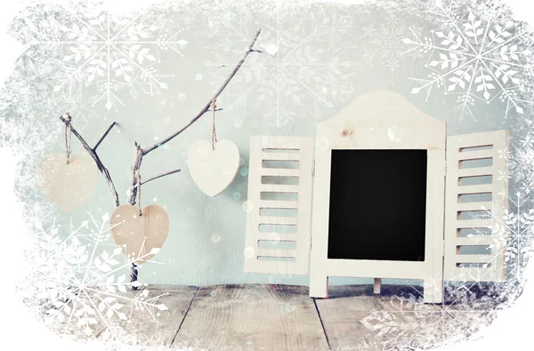 Decorative chalkboard frame and wooden hanging hearts over wooden table. ready for text or mockup. retro filtered image with snowflakes overlay. — Stock Photo, Image