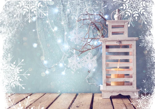 White wooden vintage lantern with burning candle and tree branches on wooden table. retro filtered image with glitter and snowflake overlay. — Zdjęcie stockowe