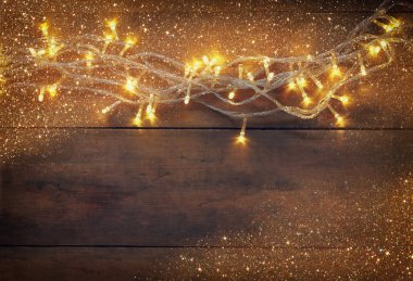 Christmas warm gold garland lights on wooden rustic background. filtered image with glitter overlay.