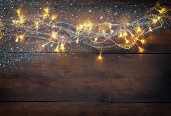 Christmas warm gold garland lights on wooden rustic background. filtered image with glitter overlay. — Stok fotoğraf